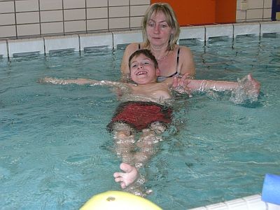 Therapeutin führt den Schüler am Kopfende auf dem Rücken liegend durch das Wasser
