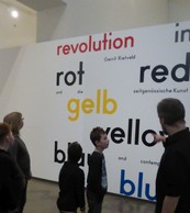 Die Schüler und Lehrerinnen der MIT A2 und der Museumsführer stehen vor dem großen Ausstellungsplakat