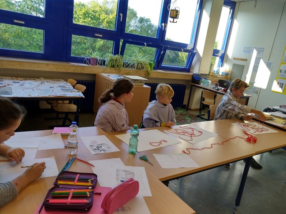 Die Schülerinnen und Schüler überlegen sich, wie der rote Faden auf ihrem Blatt liegen soll. Danach wird der Faden mit roter Farbe eingefärbt und auf das Blatt gedruckt.