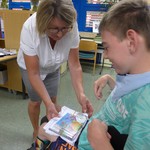 Lehrerin überreicht Schüler Buch, DVD, CD und T-Shirt (vergrößerte Bildansicht wird geöffnet)