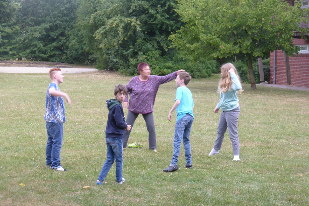 Eine Lehrerin macht mit 4 Schülern auf der Wiese Übungen